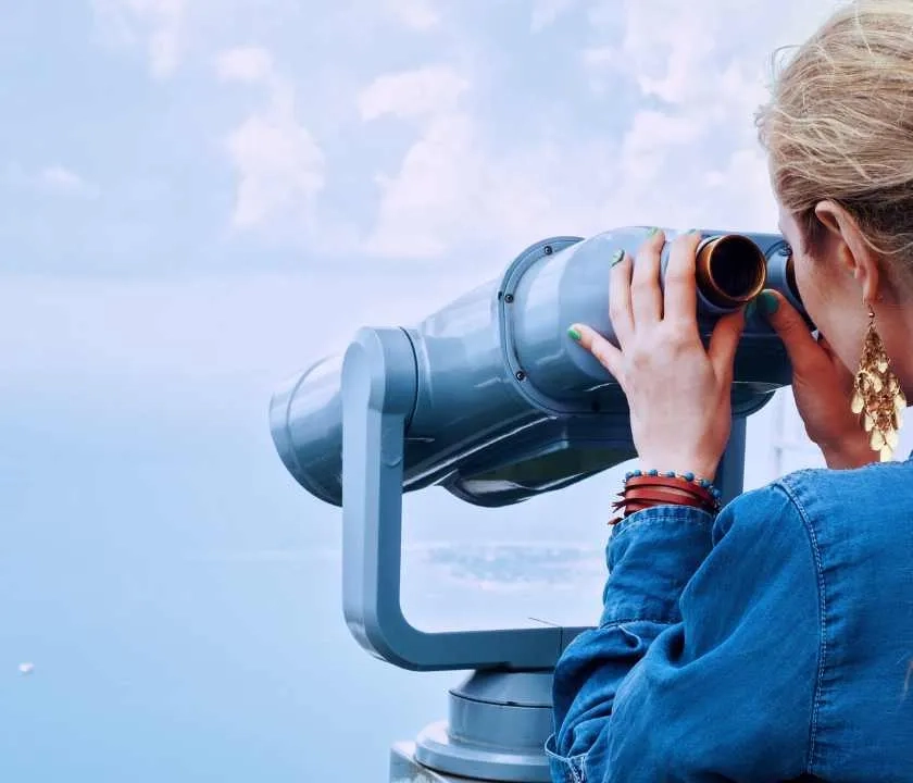 A woman peering into a telescope towards the sea